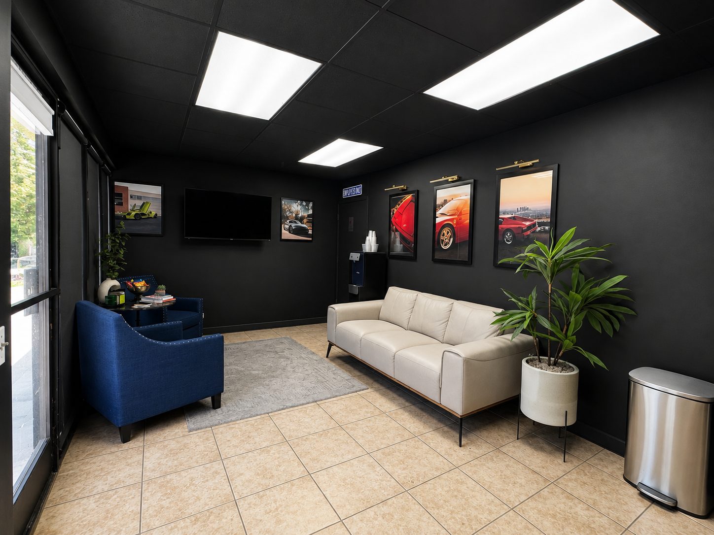 Seating area at Gravity Garage with a wall-mounted screen, framed automotive photography, and natural light from the street-facing windows.